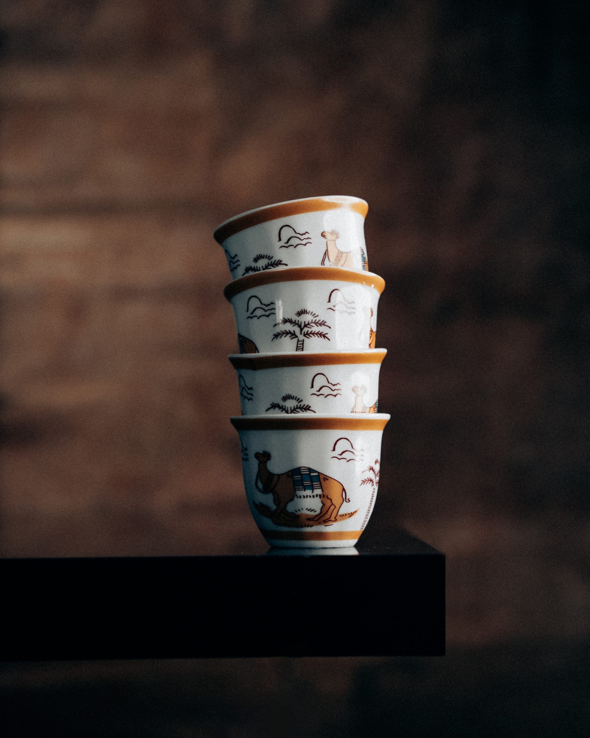 Four hand-painted finjan cups stacked on a dark wooden shelf