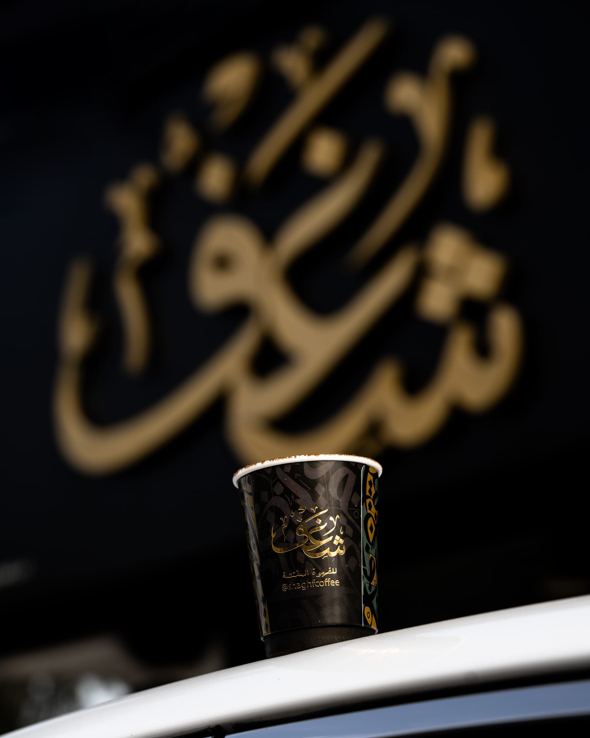 A Shaghf cup in front of the gold Arabic sign of a cafe